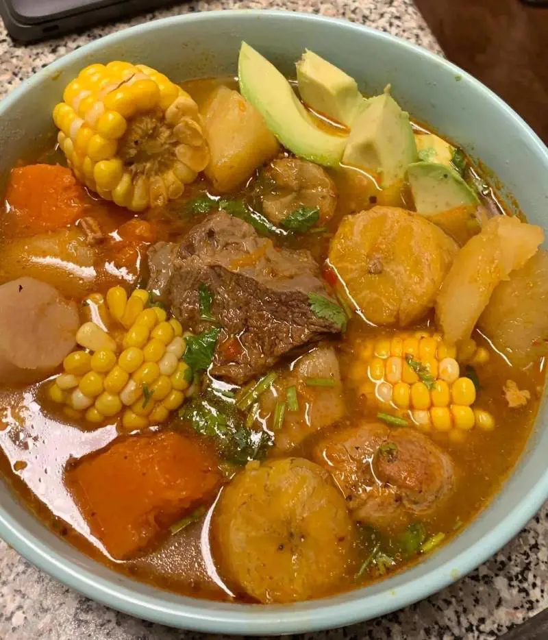 Sancocho is a traditional stew served with a small bowl of rice, pique criollo, tostones, and bread